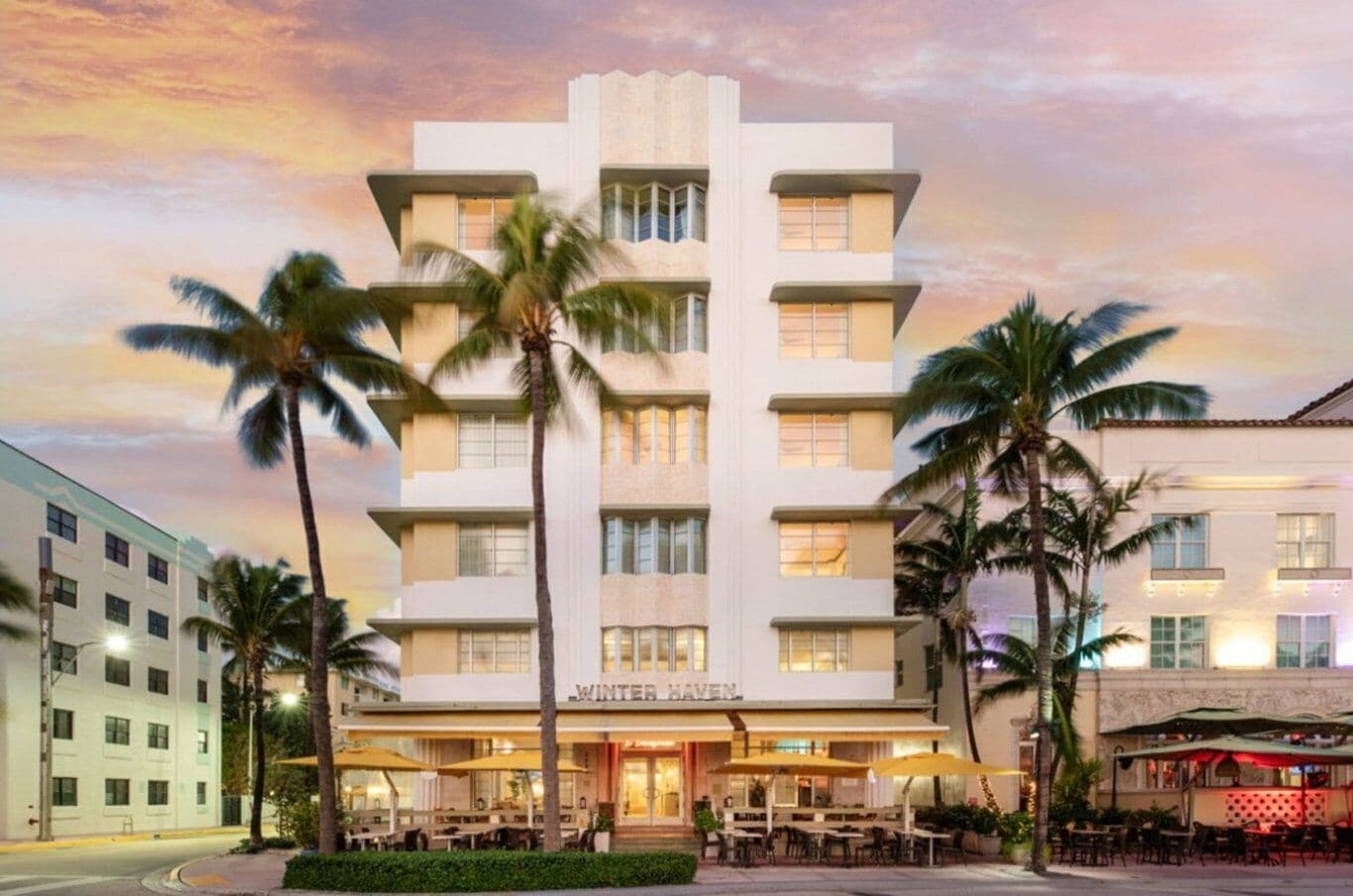 A multi-story hotel with a flat facade, palm trees in front, and outdoor seating.