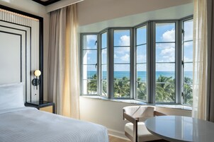 A hotel room with a large bay window offering a view of the ocean and palm trees.