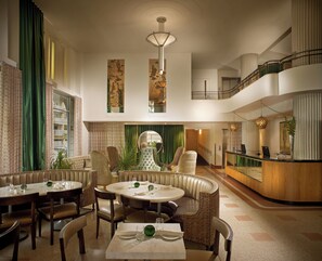 En rymlig hotellobby med en central sittgrupp, en receptionsdisk och en trappa som leder upp till en övre våning.