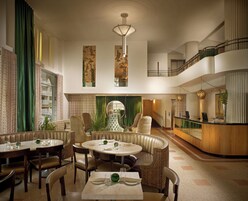 A spacious hotel lobby with a central seating area, a reception desk, and a staircase leading to an upper level.