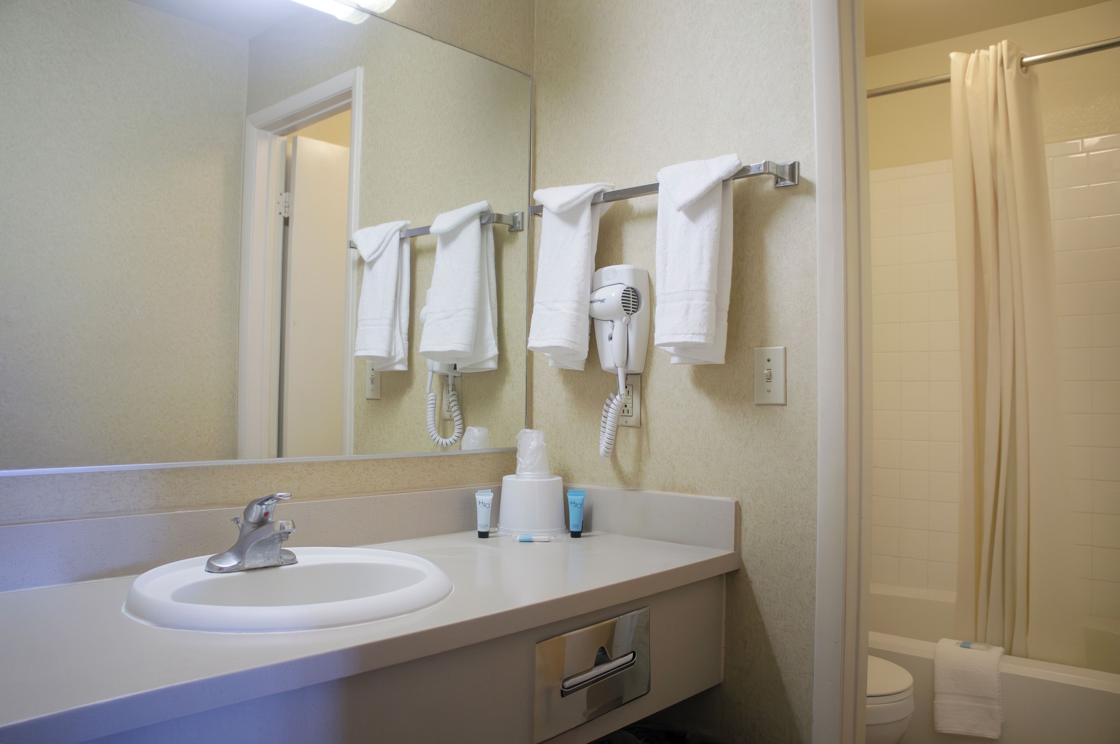 A bathroom with a sink, mirror, towel rack, hairdryer, and shower curtain.