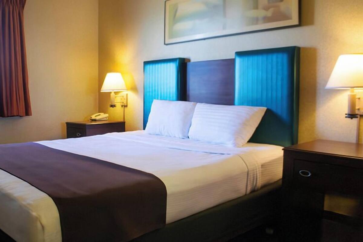 A hotel room with a large bed, two bedside tables, a window with curtains, and a painting on the wall.