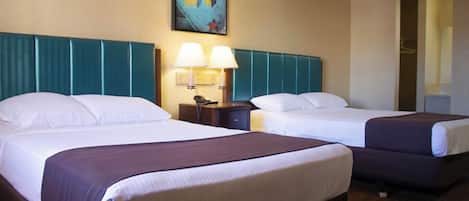 Quarto de hotel com duas camas, cabeceira com painéis azul-turquesa, um quadro na parede e mesa de cabeceira com luminária.