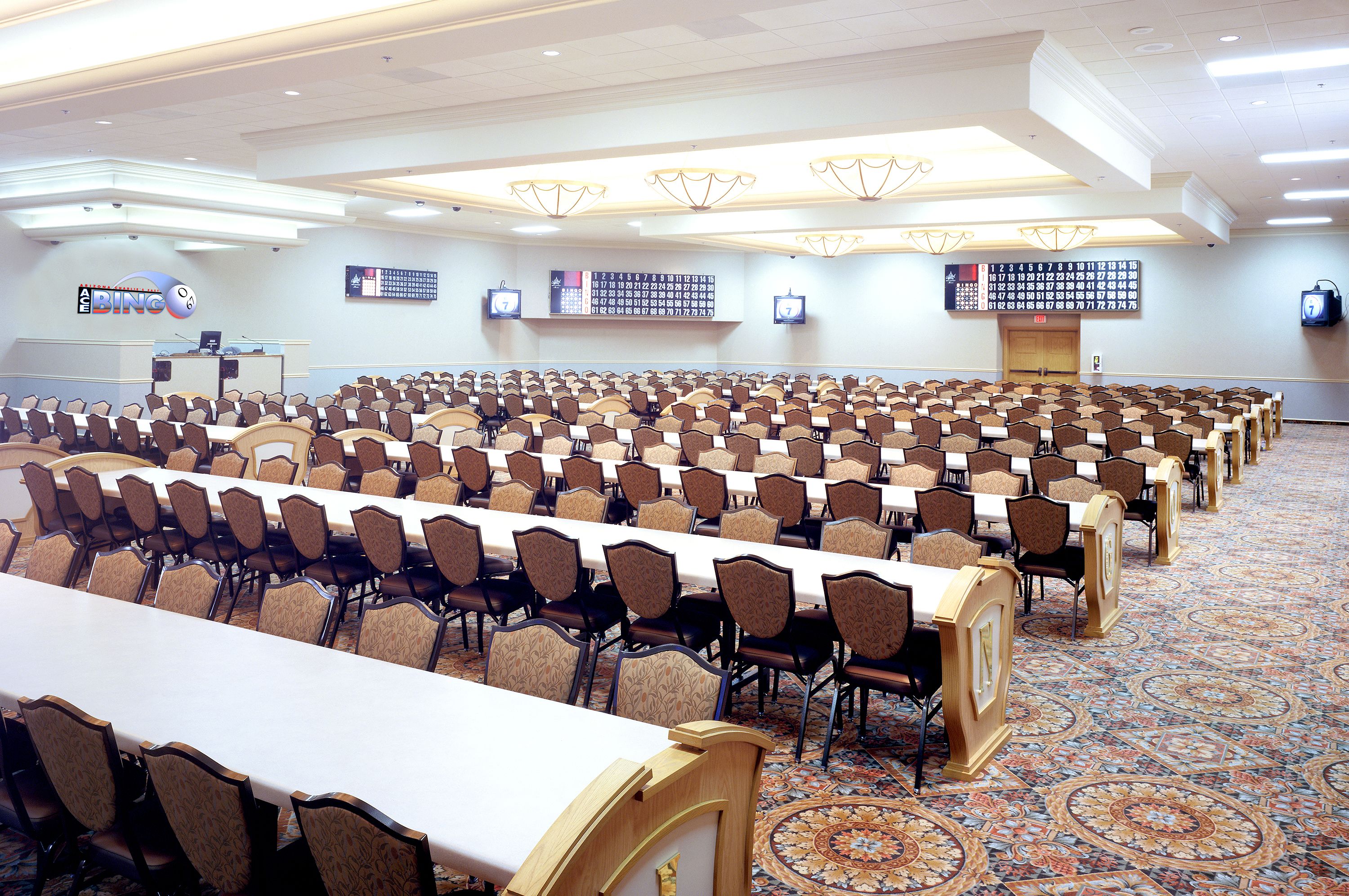 A conference room with rows of tables and chairs, a podium, and a large digital display on the wall.