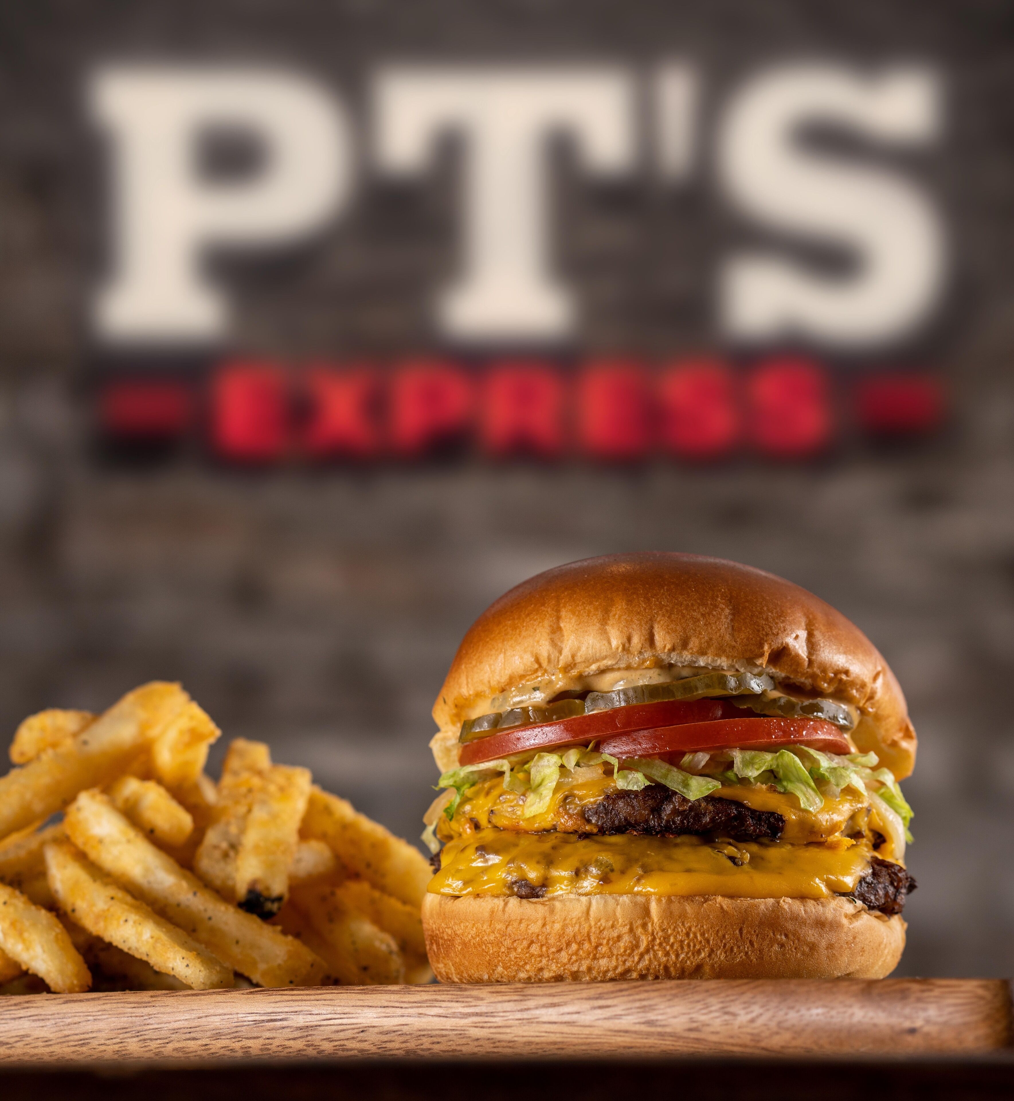 Un hamburger accompagné de frites, avec en arrière-plan une enseigne indiquant « PT'S EXPRESS ».
