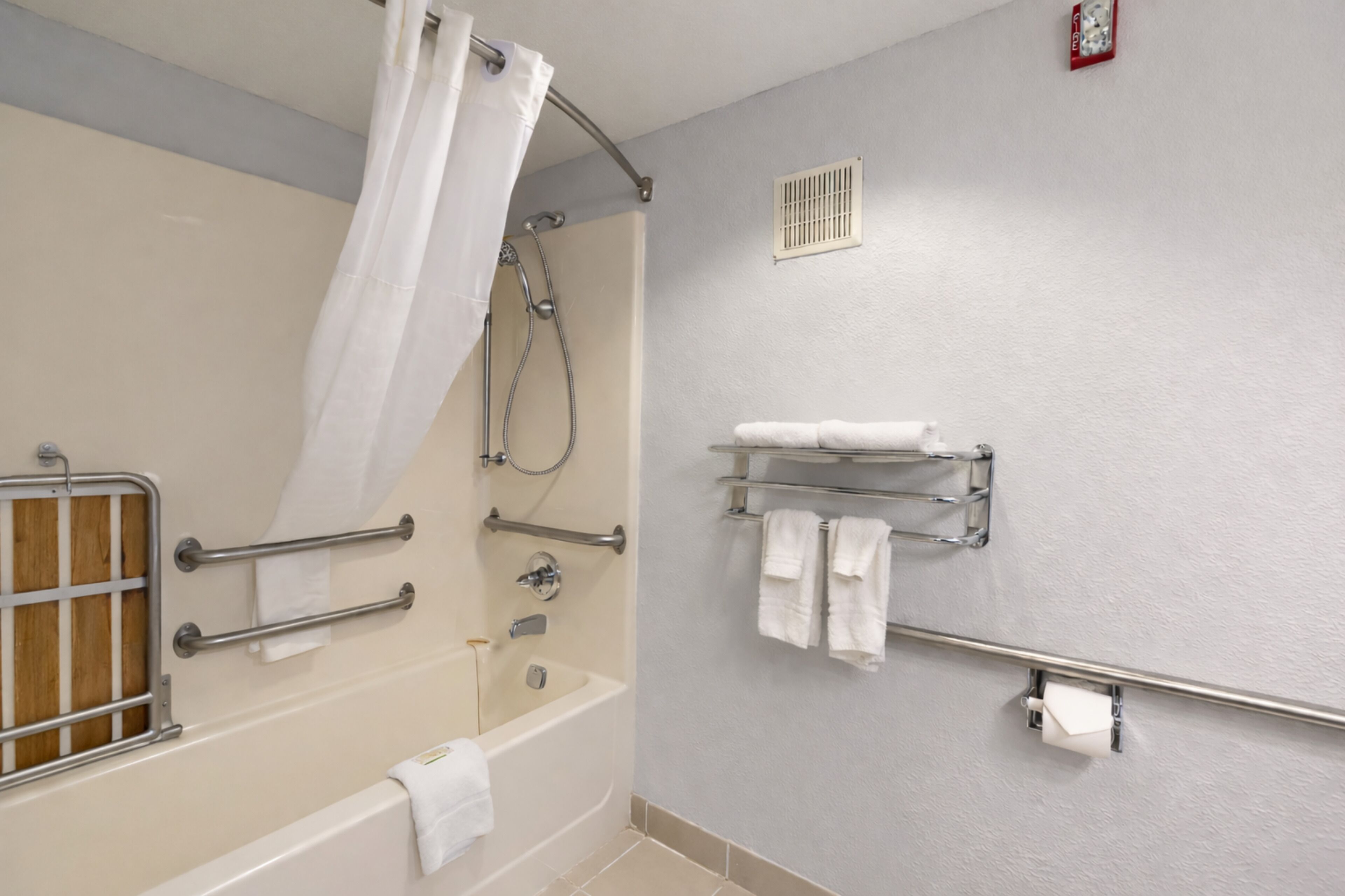 A bathroom with a bathtub, shower, grab bars, a towel rack, and a toilet paper holder.