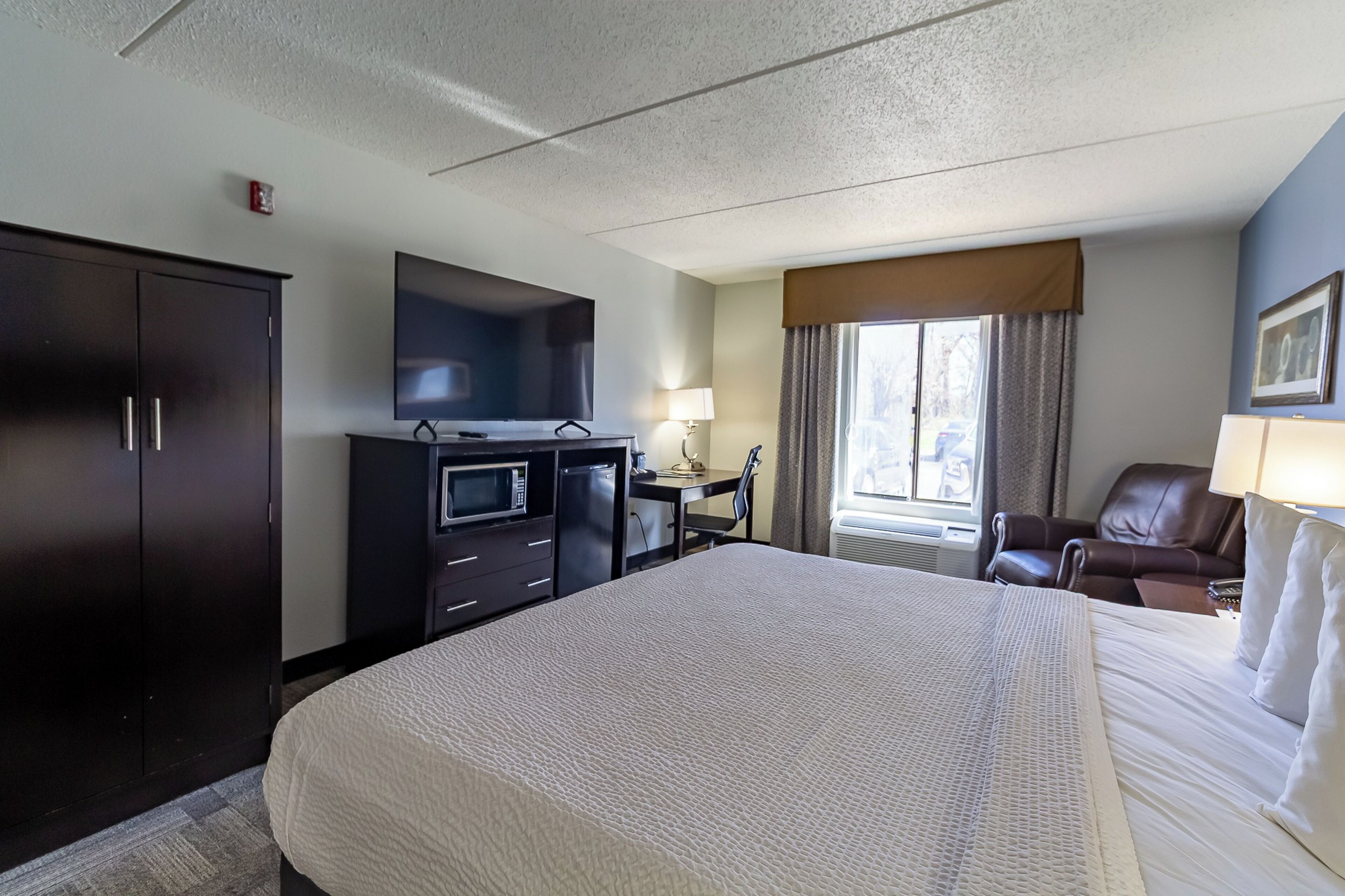 A hotel room with a large bed, a desk with a chair, a television, a wardrobe, and a window with curtains.