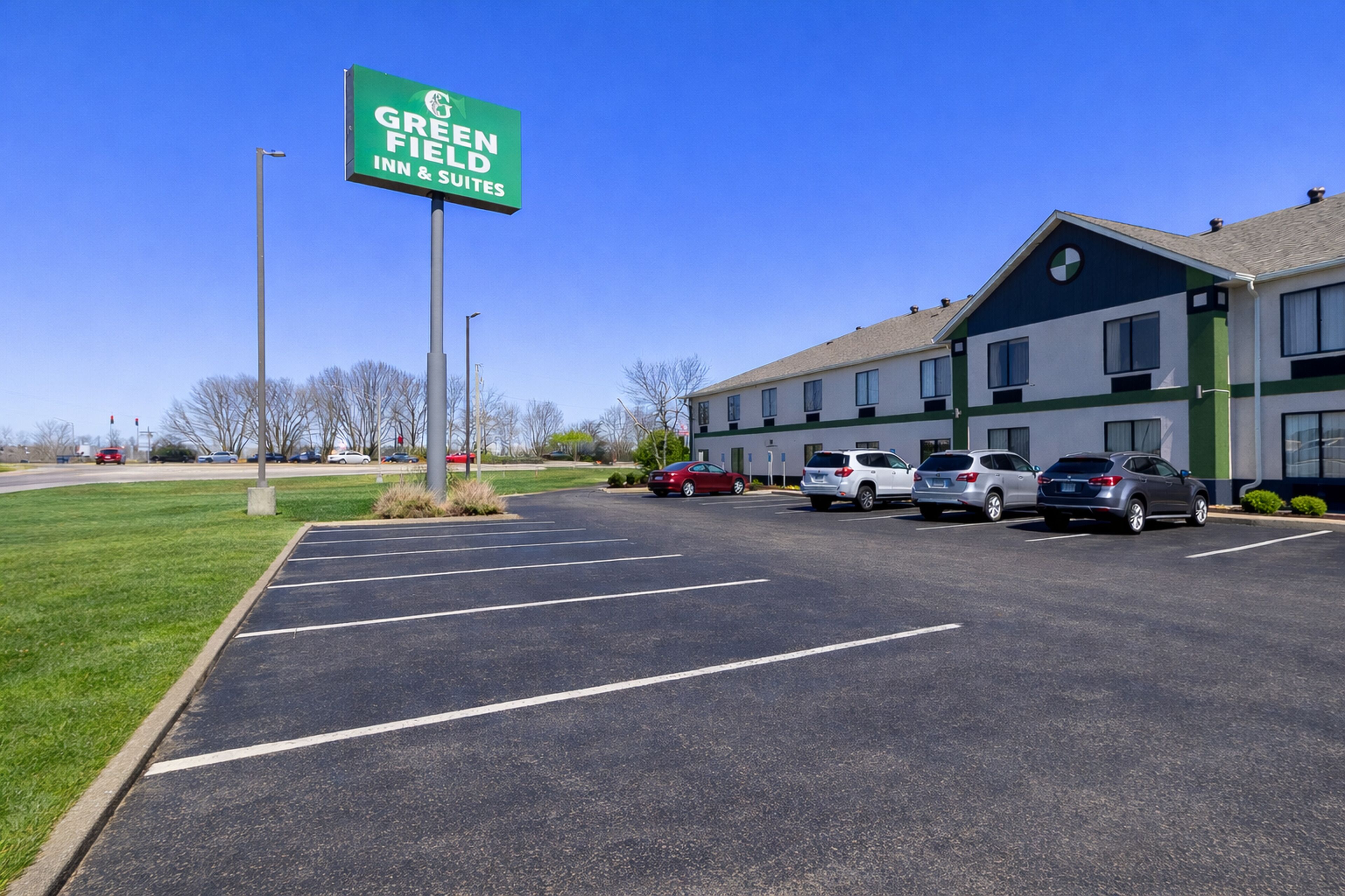 A Greenfield Inn & Suites with a parking lot, multiple cars, and a building with a green and white color scheme.
