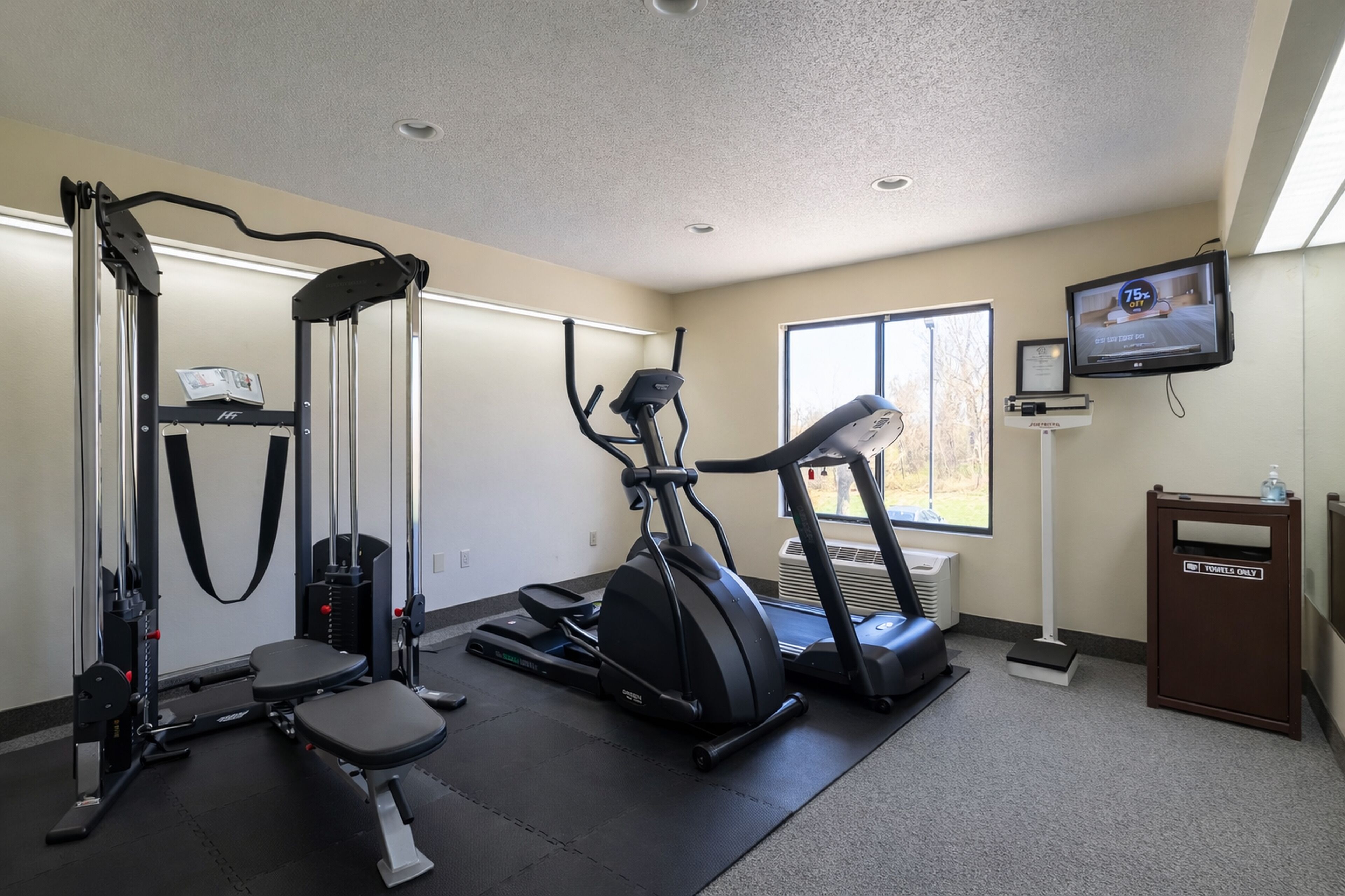 A gym with cardio machines, a weight machine, and a television displaying a fitness program.