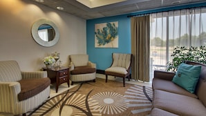 Un salón con una pared azul de acento, un espejo redondo, dos sillones a rayas, un sofá marrón, una mesa de centro y un ventanal con cortinas.