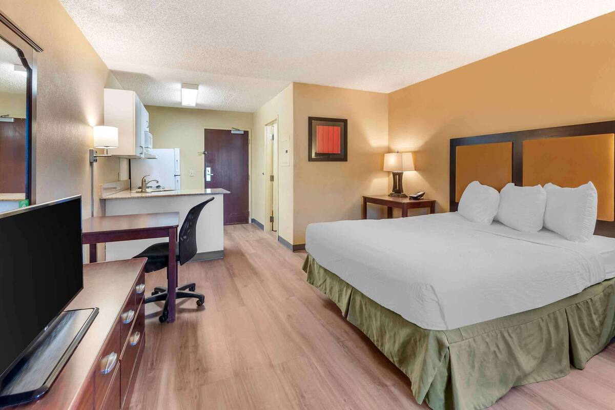 Habitación de hotel con cama, escritorio, silla y una kitchenette pequeña.