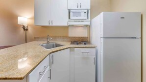 A compact kitchen with white cabinets, a microwave, a stove, and a refrigerator.
