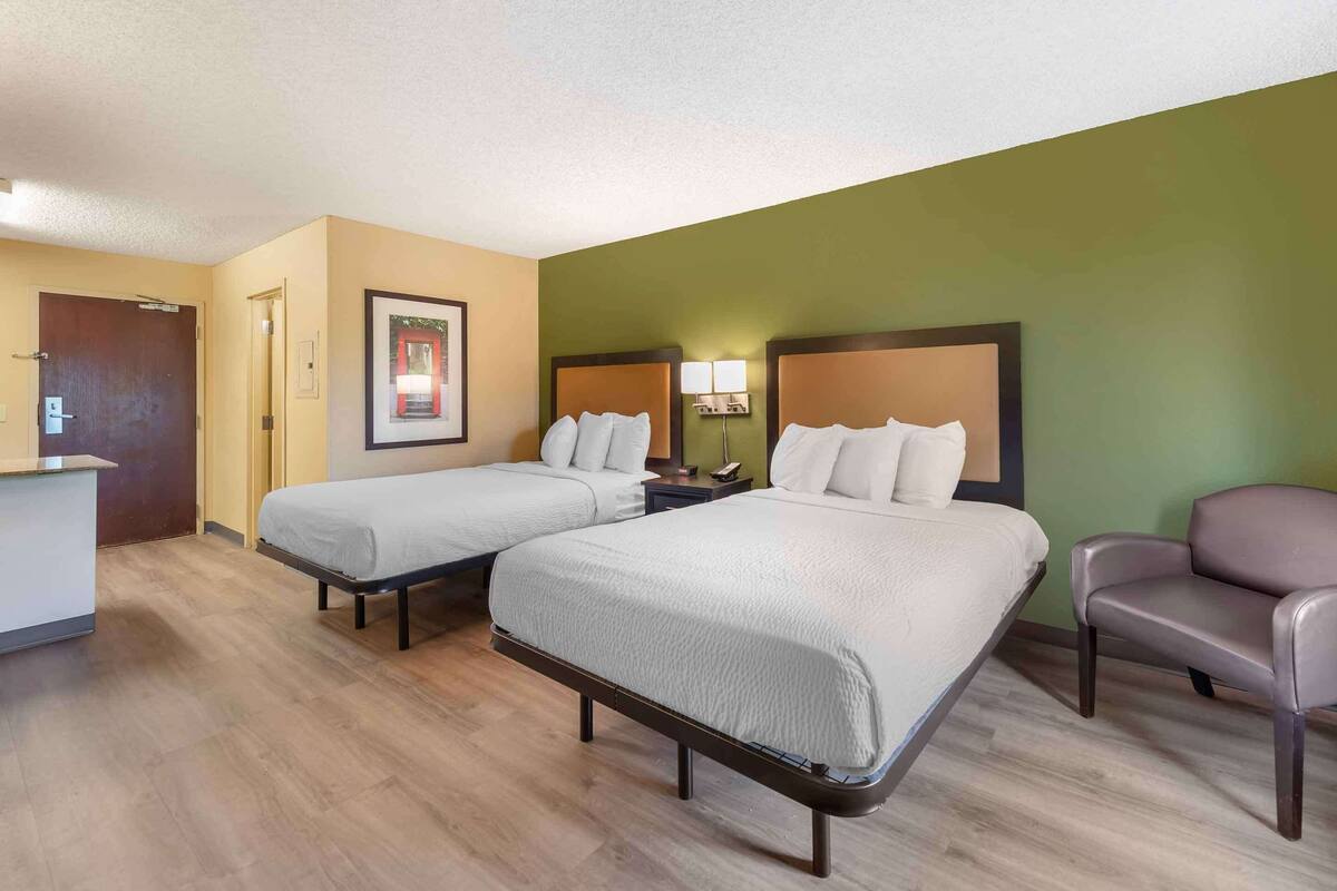 Habitación de hotel con dos camas, un escritorio, una silla y una pared decorada en color verde.