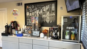 A breakfast bar with a large sign reading "Greetings from California," a coffee machine, a refrigerator, and a television mounted on the wall. - Super 8 by Wyndham Red Bluff (Red Bluff)
