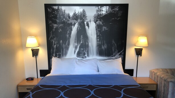 A hotel room with a bed, two bedside lamps, a digital clock, and a large framed waterfall picture on the wall. - Super 8 by Wyndham Red Bluff (Red Bluff)
