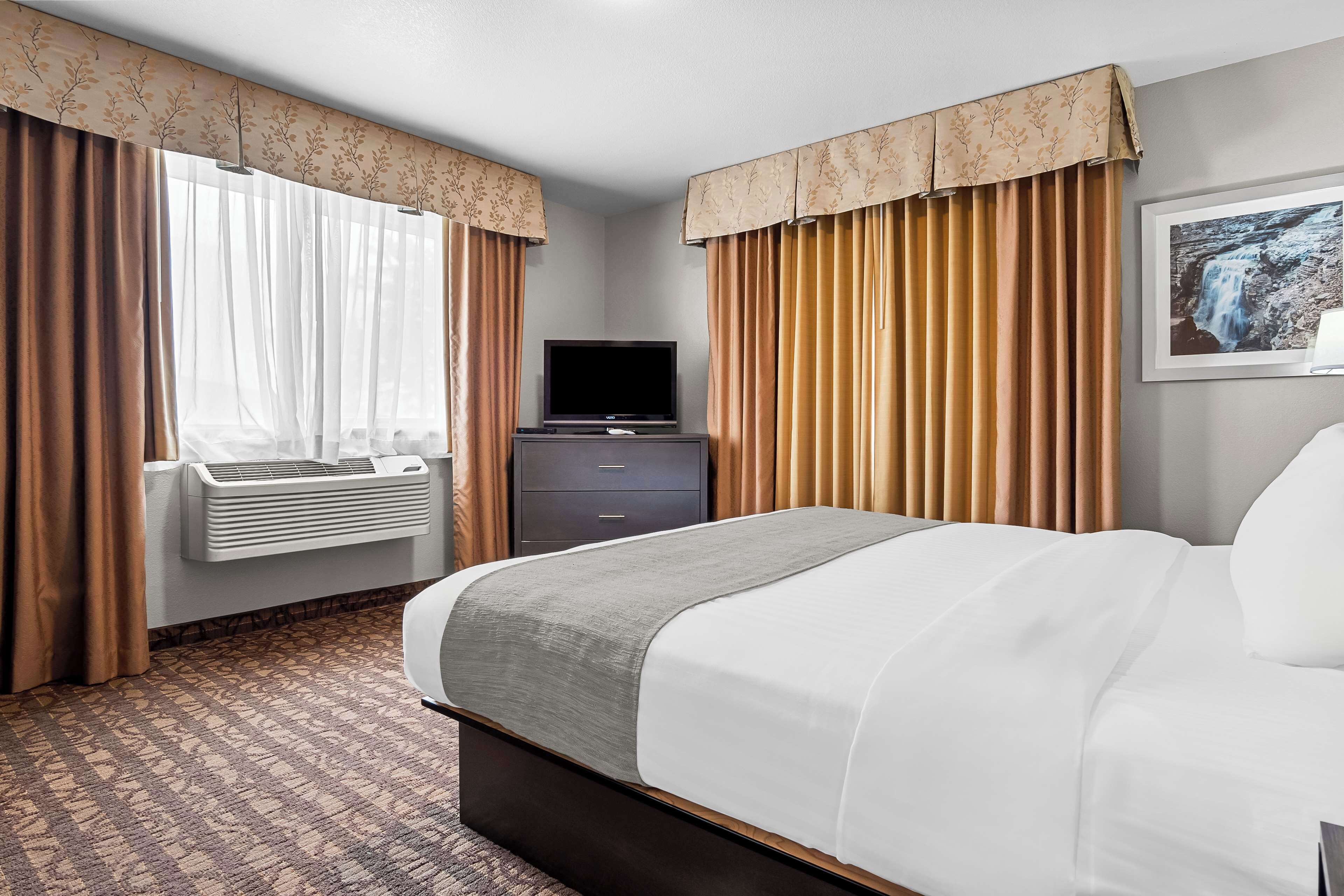 Habitació d'hotel amb un llit, una televisió, una petita estant i una finestra amb cortines.