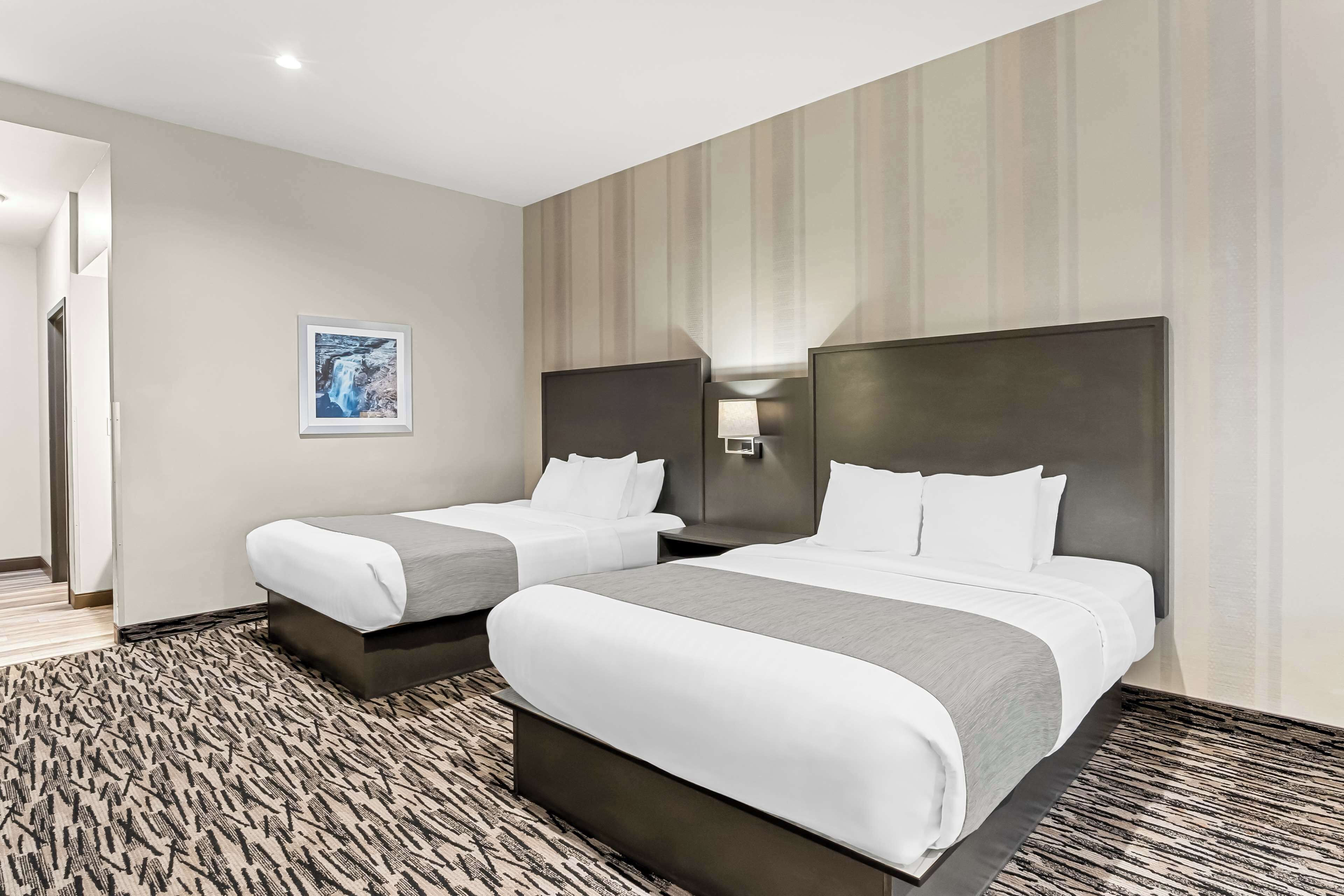 A hotel room with two beds, a large window, and a wall-mounted artwork.