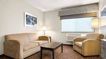 Habitación de hotel con sofá color beige, una mesita, un sillón estampado, una lámpara y una ventana con vistas.
