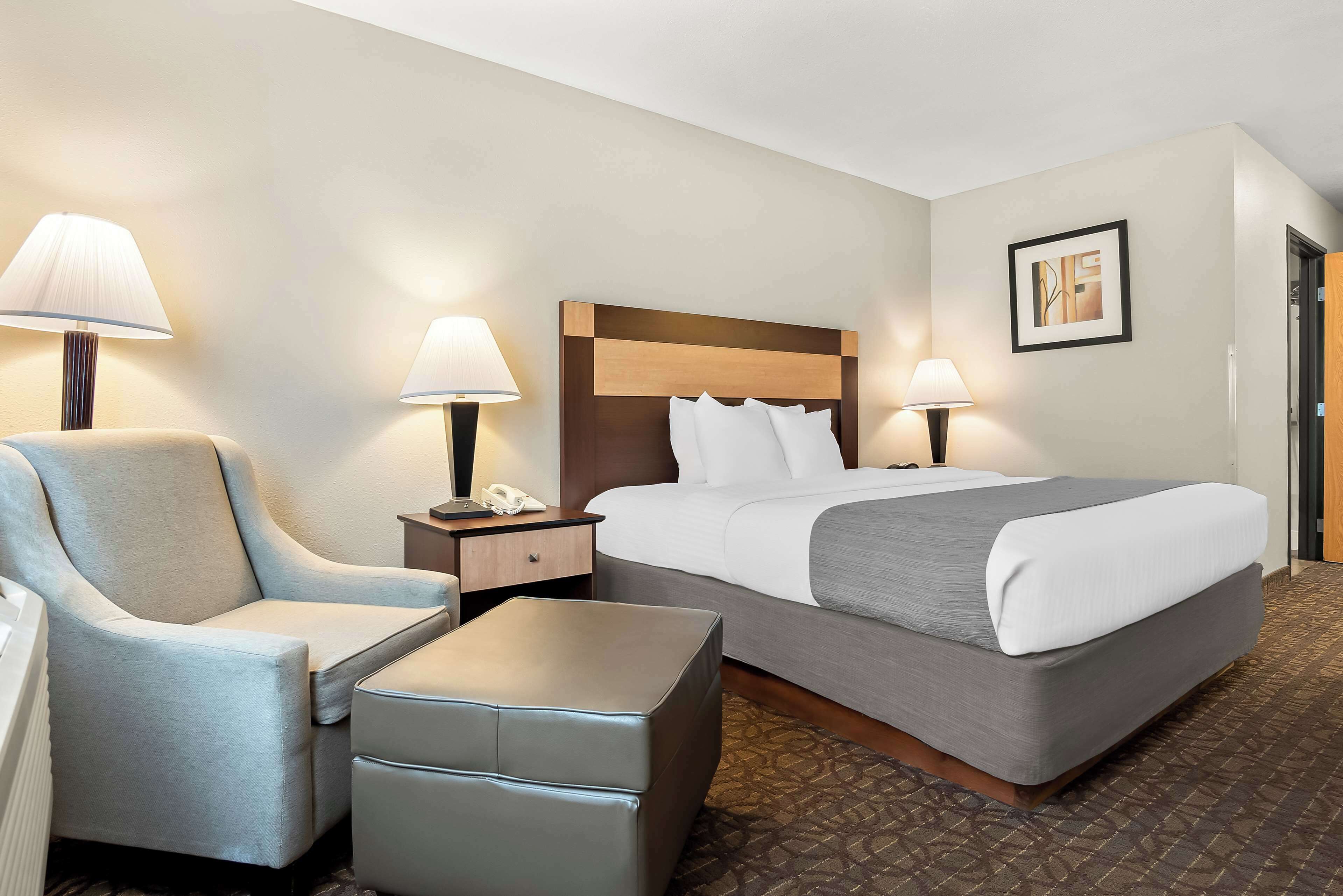 A hotel room with a large bed, two bedside tables with lamps, a chair, and a small ottoman.