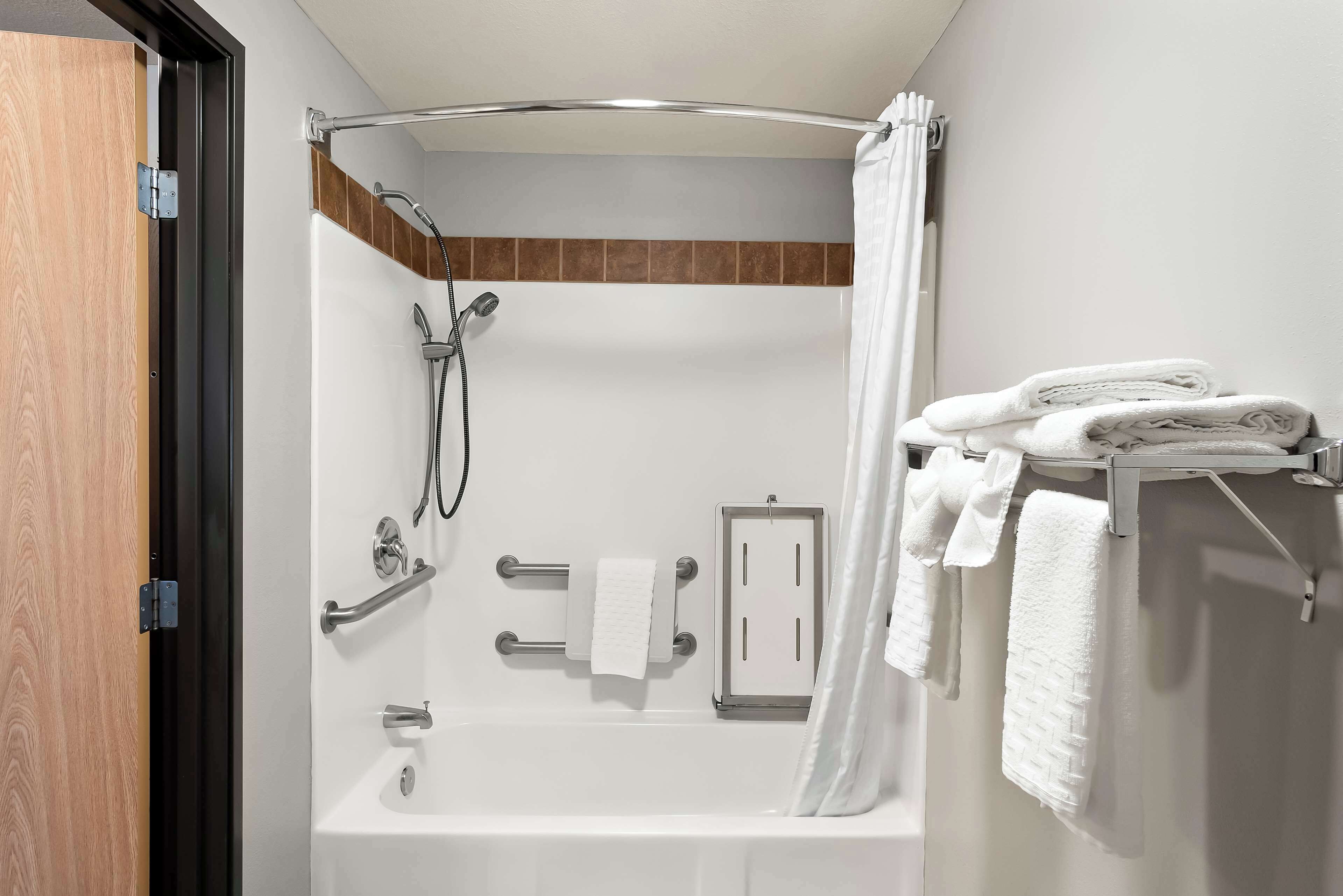 Une salle de bain moderne équipée d’une douche, de barres d’appui, d’un porte-serviettes et d’un support à papier toilette.