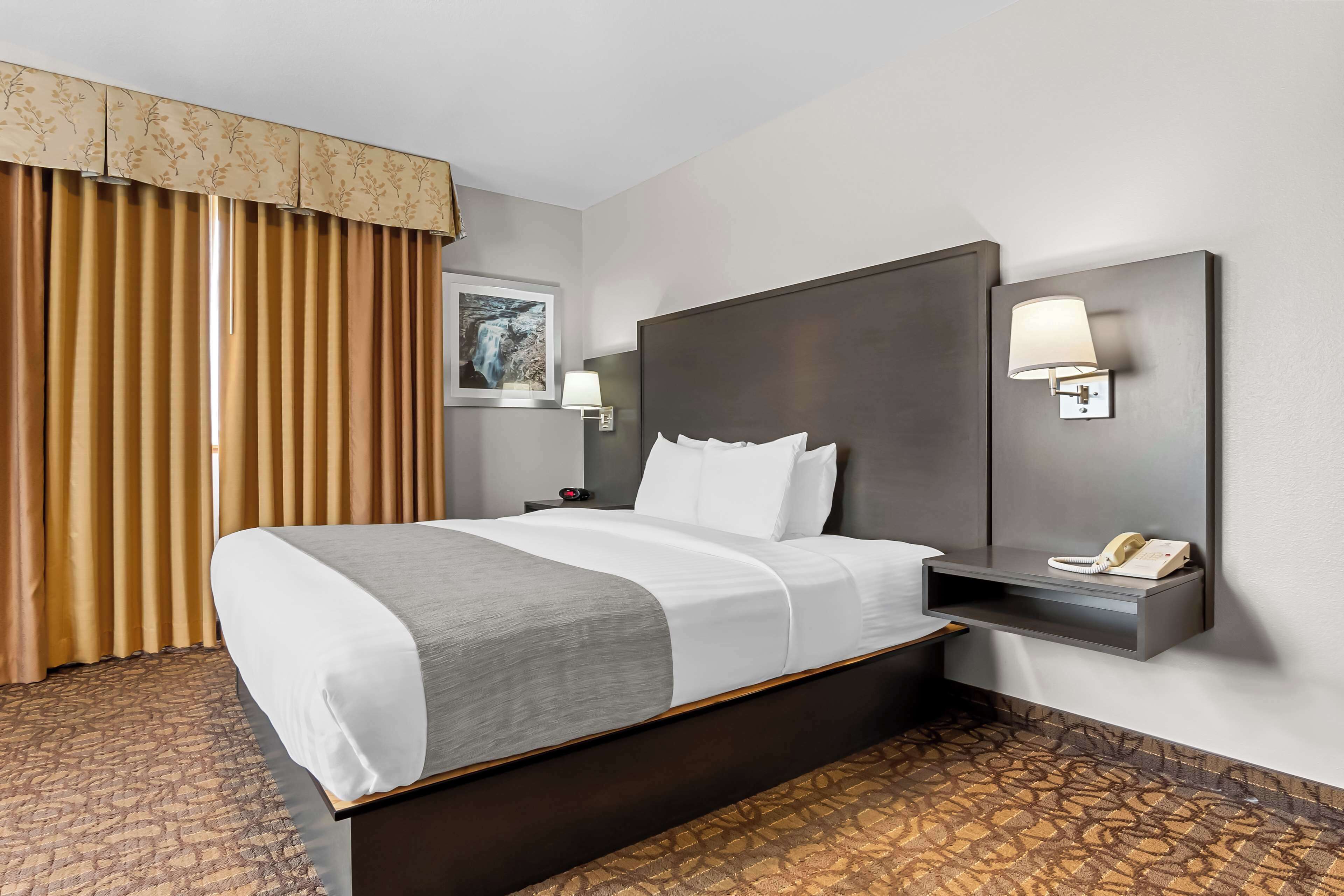A hotel room with a large bed, a nightstand, a telephone, and a wall-mounted lamp.