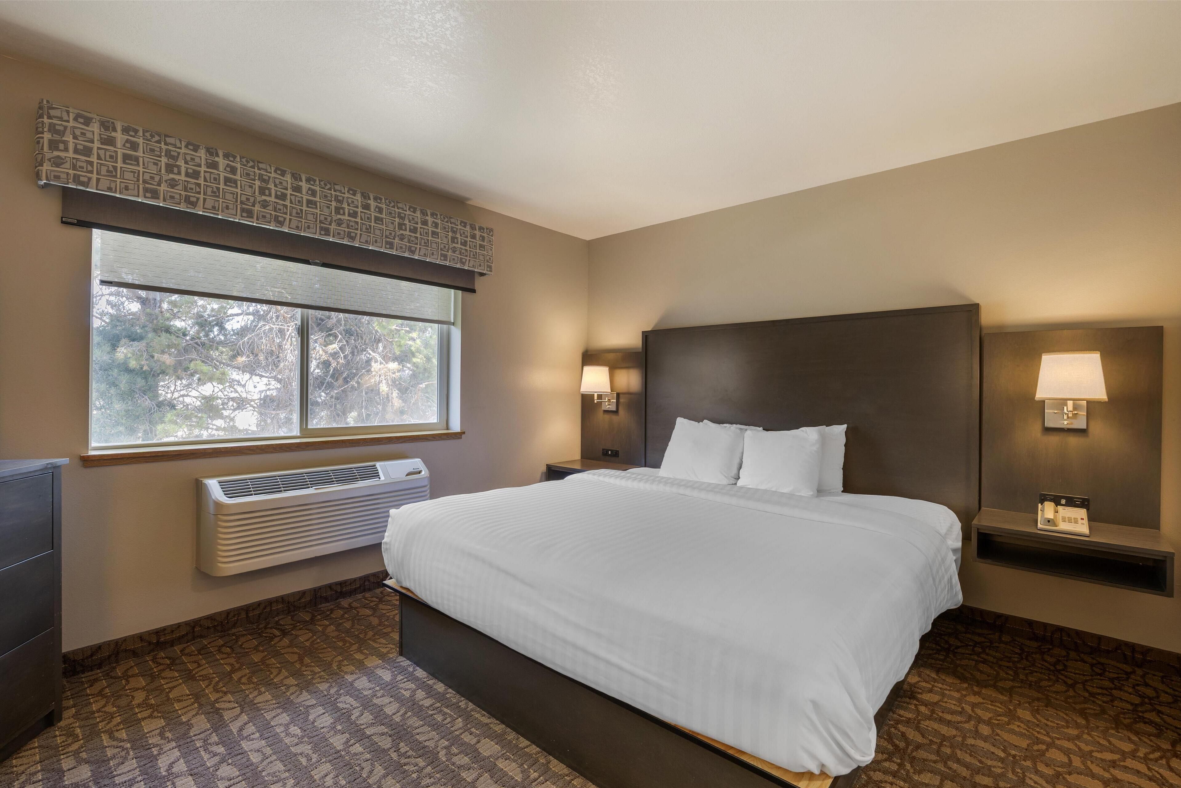A hotel room with a large bed, a window with blinds, a wall-mounted heater, and two bedside lamps.