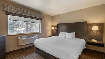 A hotel room with a large bed, a window with blinds, a wall-mounted heater, and two bedside lamps.