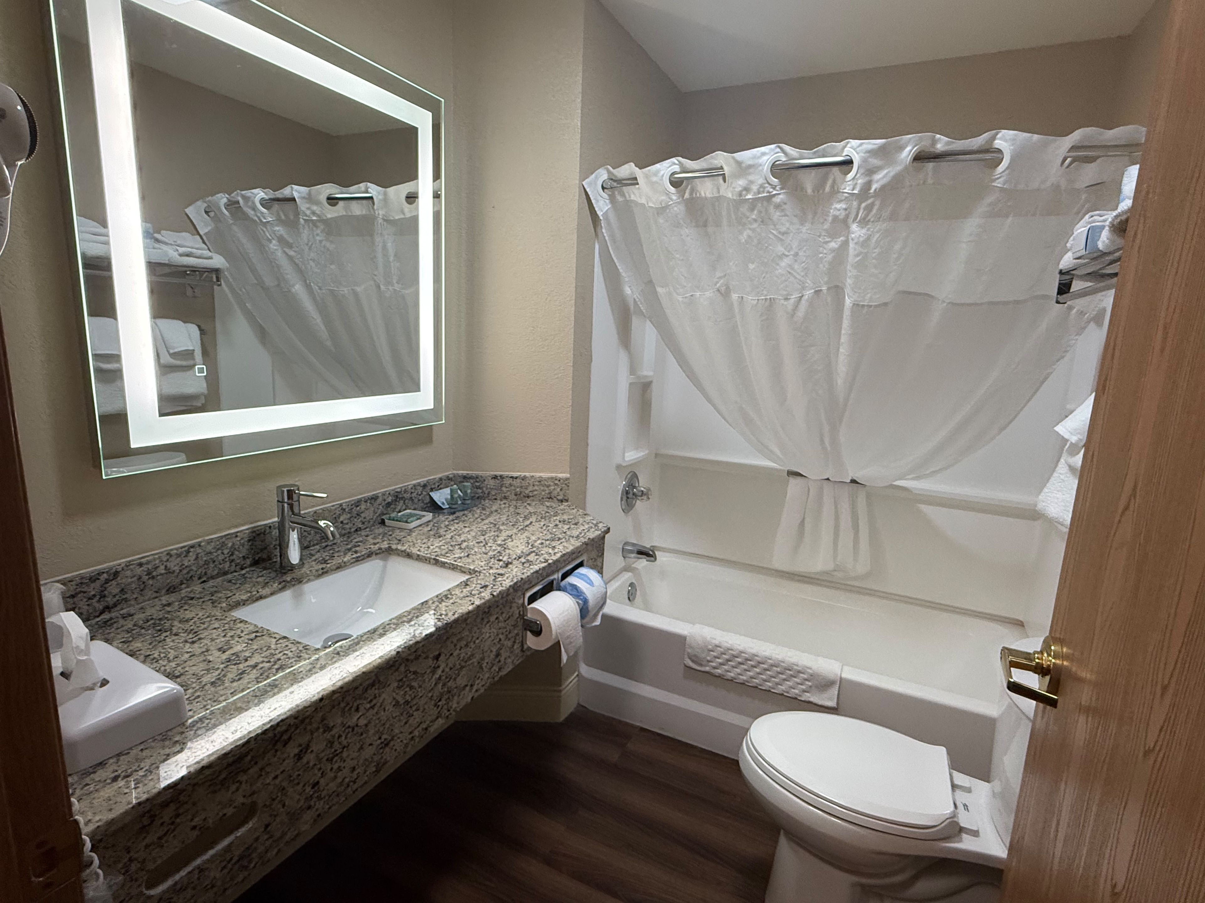 A bathroom with a granite countertop sink, a mirror, a toilet, and a bathtub with a shower curtain.