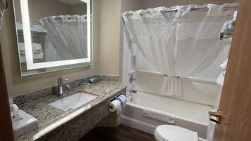 A bathroom with a granite countertop sink, a mirror, a toilet, and a bathtub with a shower curtain.