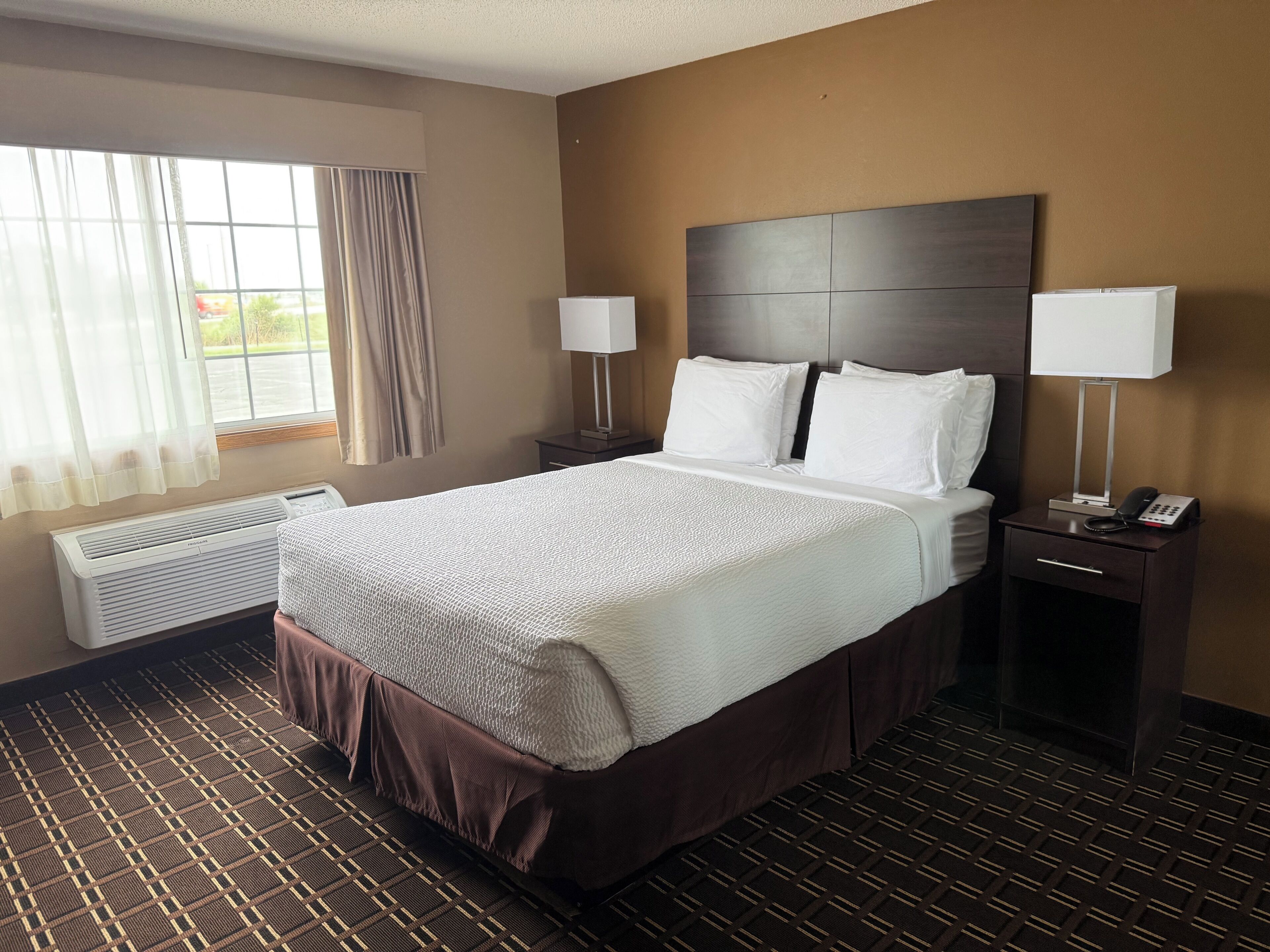 A hotel room with a large bed, two bedside tables with lamps, a heater, and a window with curtains.