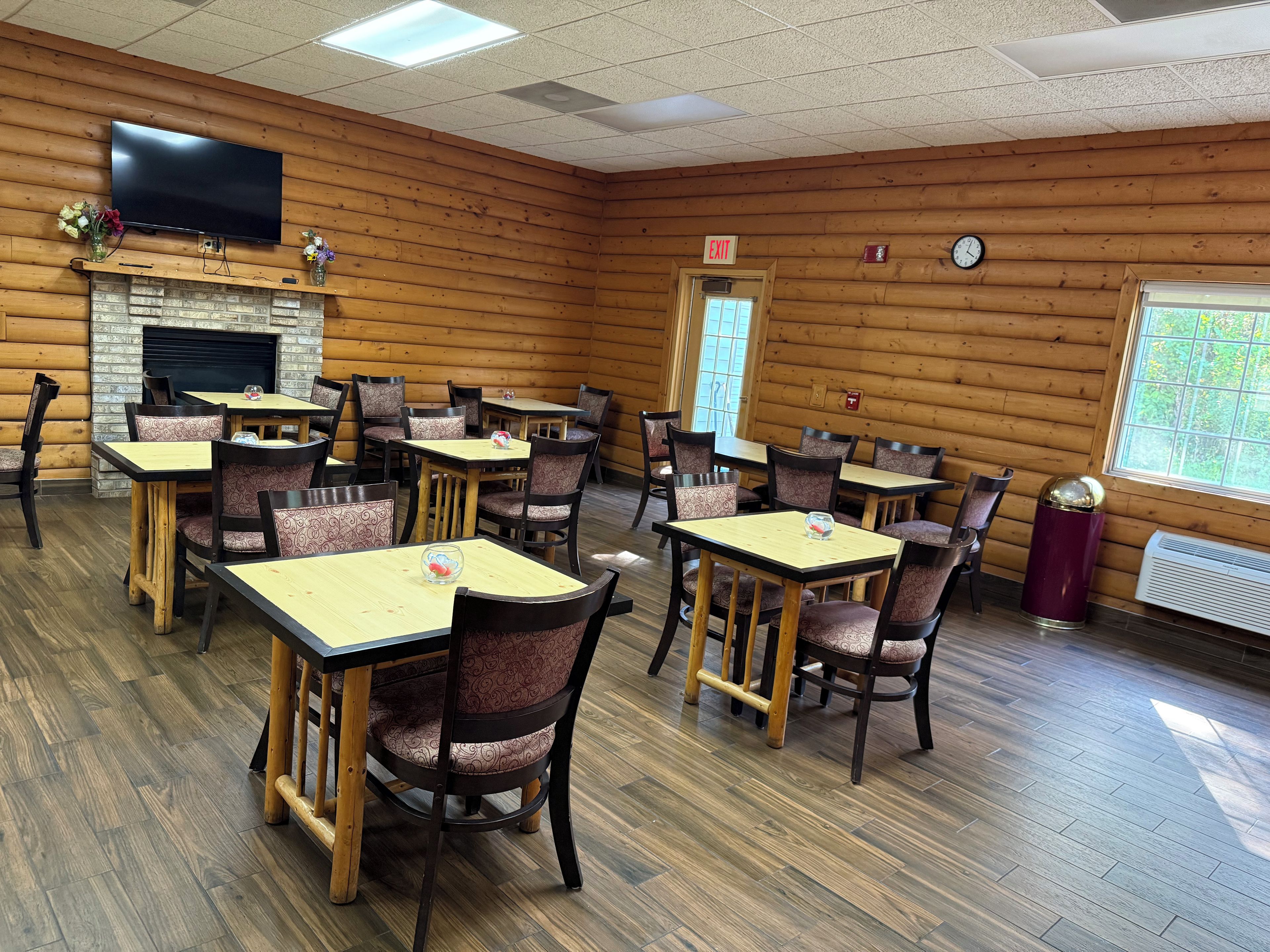 Un restaurante con paredes de madera, varias mesas y sillas, un televisor de pantalla plana, una chimenea y una señal de salida.