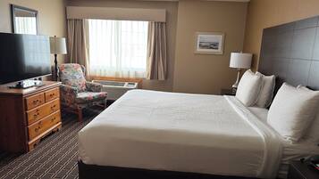 Une chambre d’hôtel avec un grand lit, une télévision, une commode, une chaise et une fenêtre avec des rideaux.