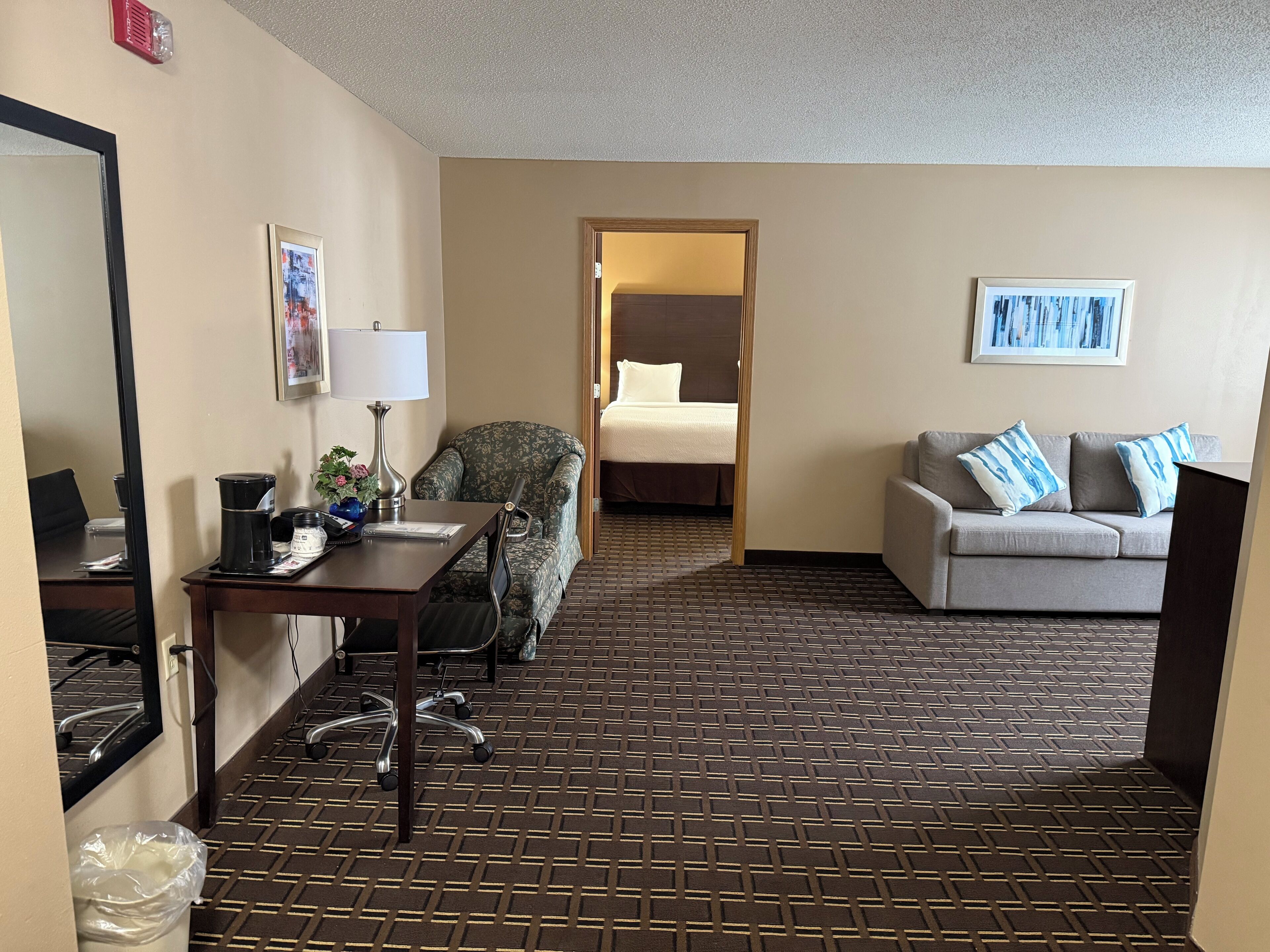 Une chambre d’hôtel avec un lit, un canapé, un bureau avec une lampe et une chaise.