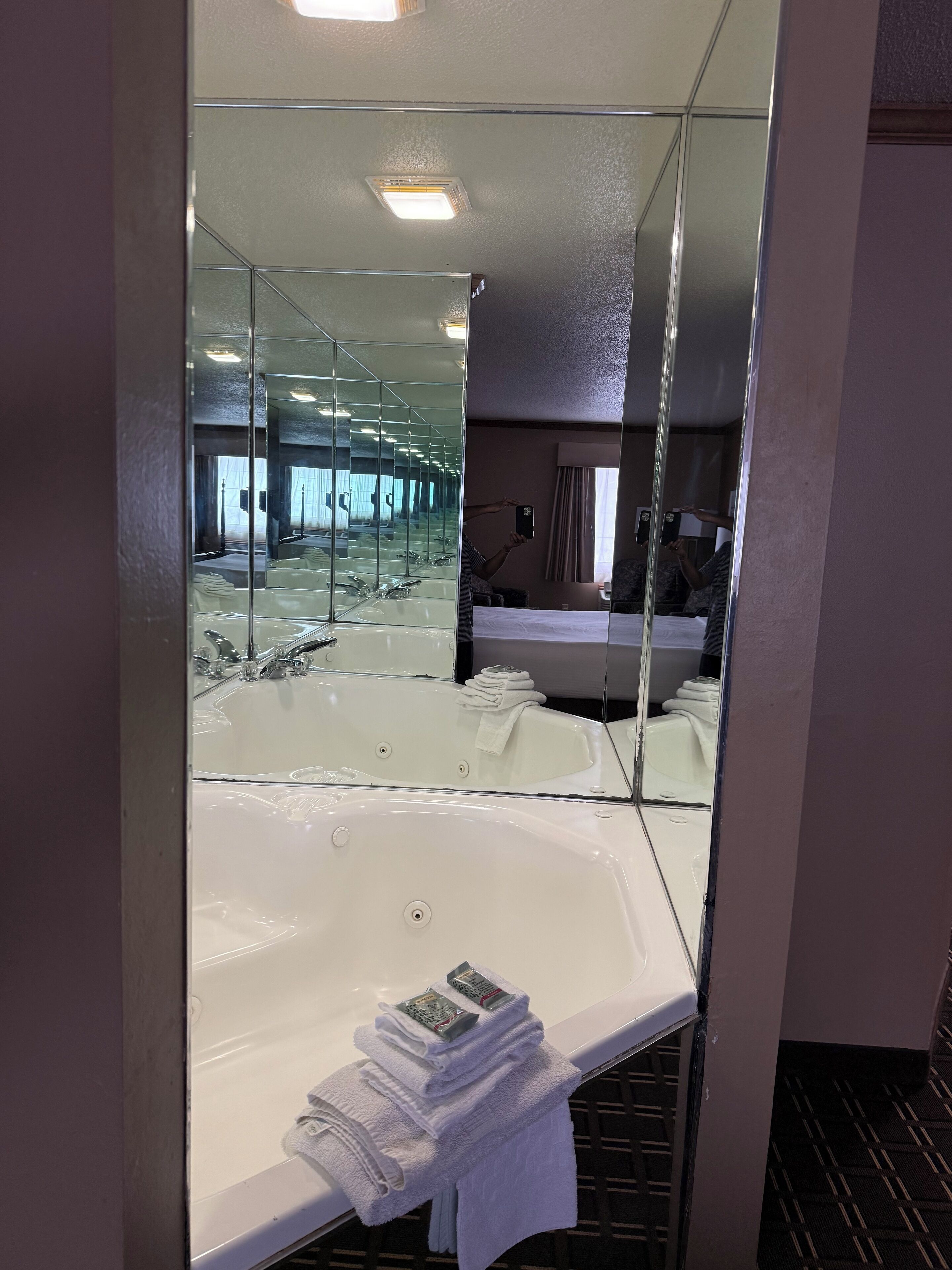 A hotel bathroom with a large mirror, a bathtub, and a sink.