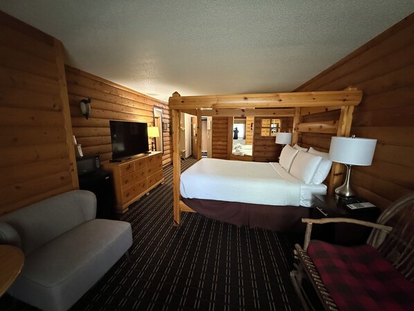 Una habitación tipo cabaña de madera con una cama, un televisor, un sofá y una silla.