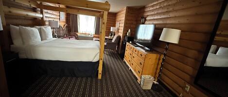 A wooden cabin-style room with a bed, dresser, television, and a window with curtains.