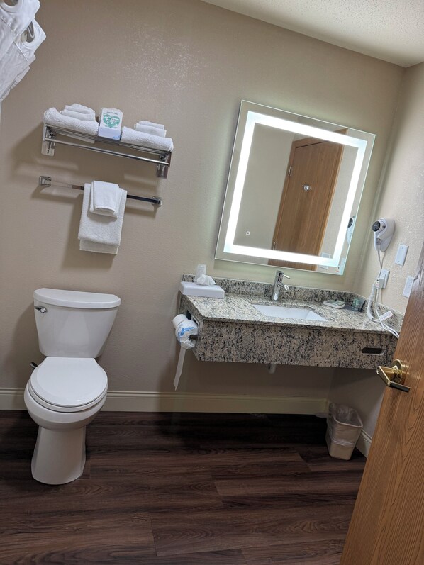 A bathroom with a toilet, a sink with a granite countertop, a mirror with lighting, and a towel rack with towels. - Best Western Dodgeville Inn & Suites (Dodgeville)