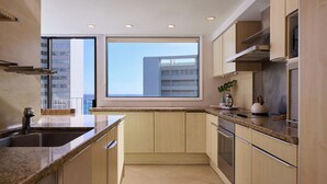 Una cocina moderna con encimeras de granito, electrodomésticos de acero inoxidable y un amplio ventanal con vistas a un edificio.