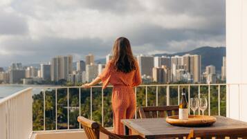 A balcony with a city view, a table with a bottle and glasses, and a chair.