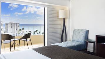 A hotel room with a balcony, a bed, a chair, a table, and a lamp.