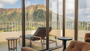 Un balcón con vistas a montañas, una silla con cojín, una mesita pequeña y barandilla de cristal.