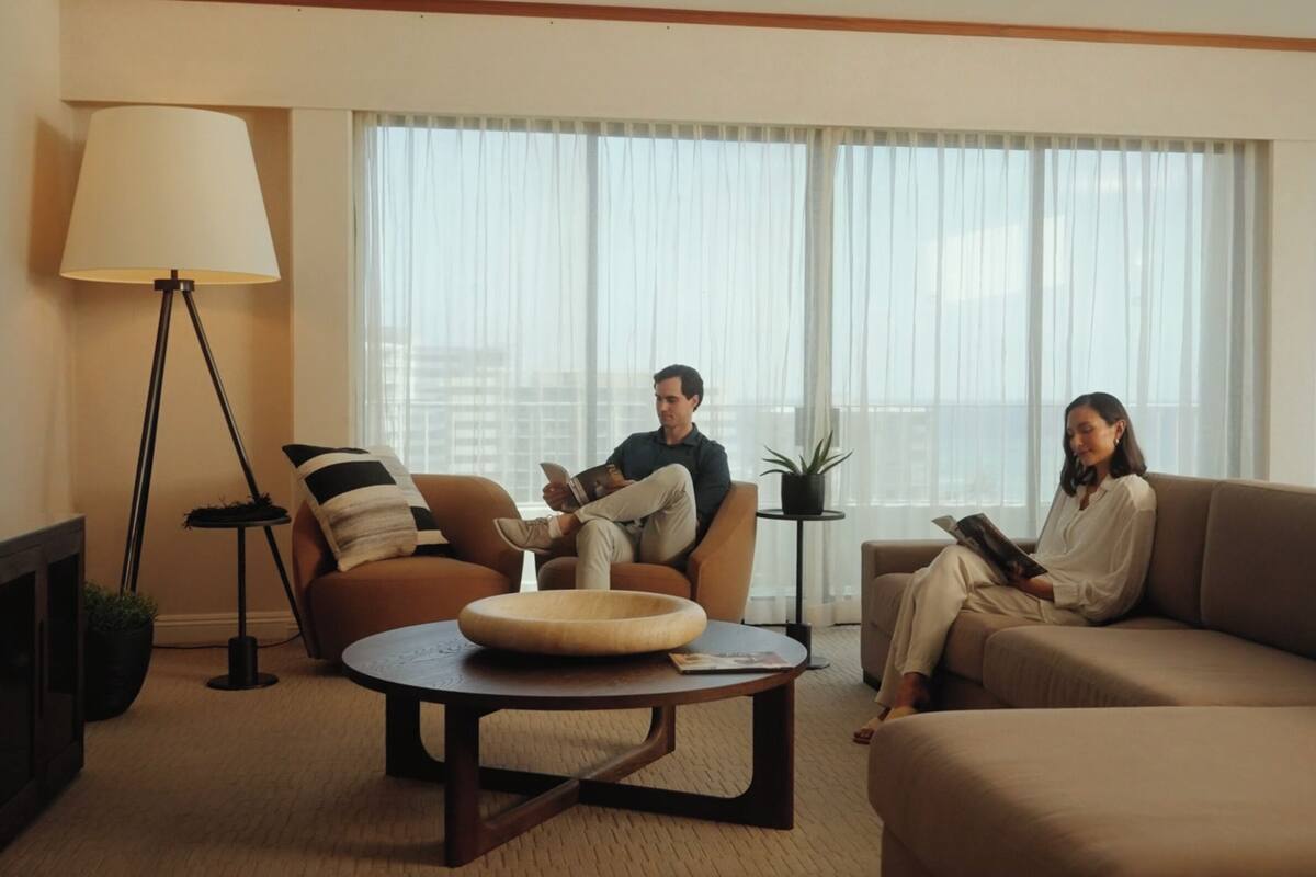A modern living room with a sofa, armchair, and coffee table. There is a floor lamp and a TV on a stand.
