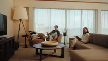 Una sala moderna con sofá, sillón y mesa de centro. Hay una lámpara de pie y un televisor sobre un mueble.