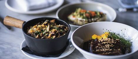 A table with three bowls of food, a wooden-handled pan, and a white plate with a napkin.
