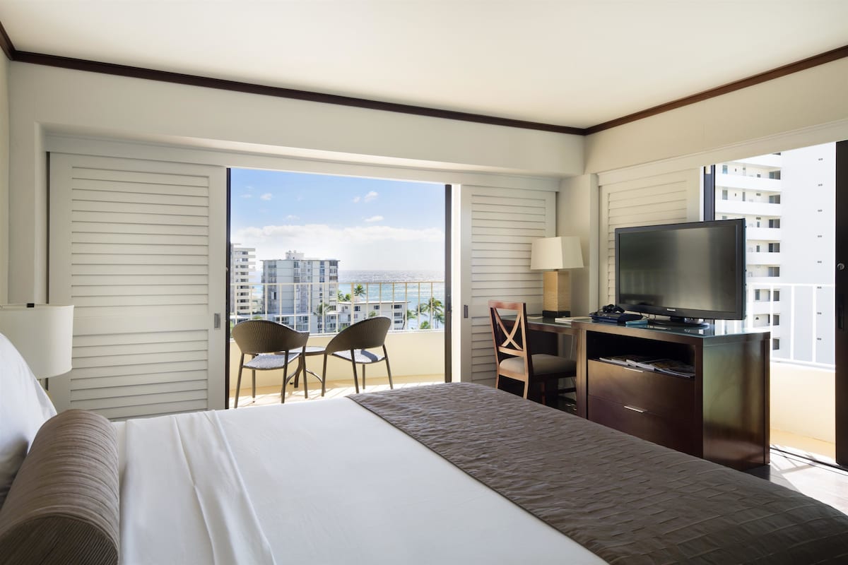 A hotel room with a bed, a desk, a television, and a view of the cityscape.