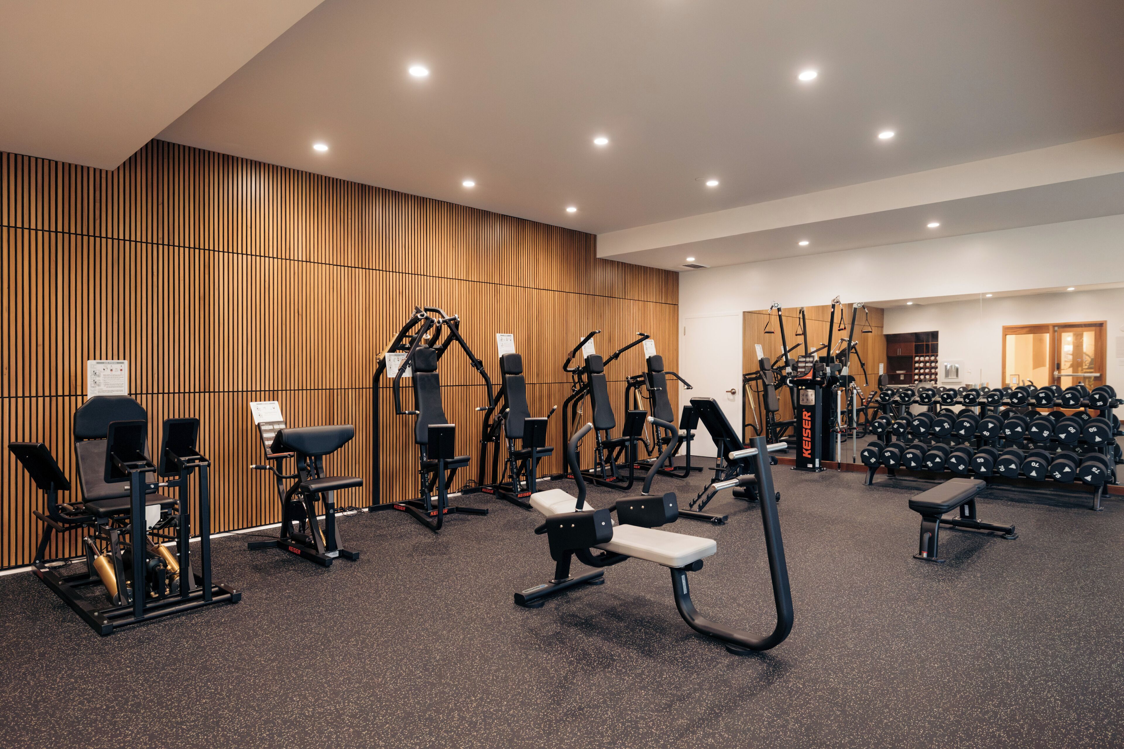 A gym with various exercise equipment, a wall-mounted mirror, and a rack of dumbbells.