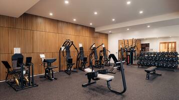 A gym with various exercise equipment, a wall-mounted mirror, and a rack of dumbbells.
