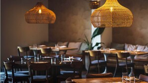 Interior de restaurante con lámparas colgantes de mimbre, mesas de madera y asientos acolchados.