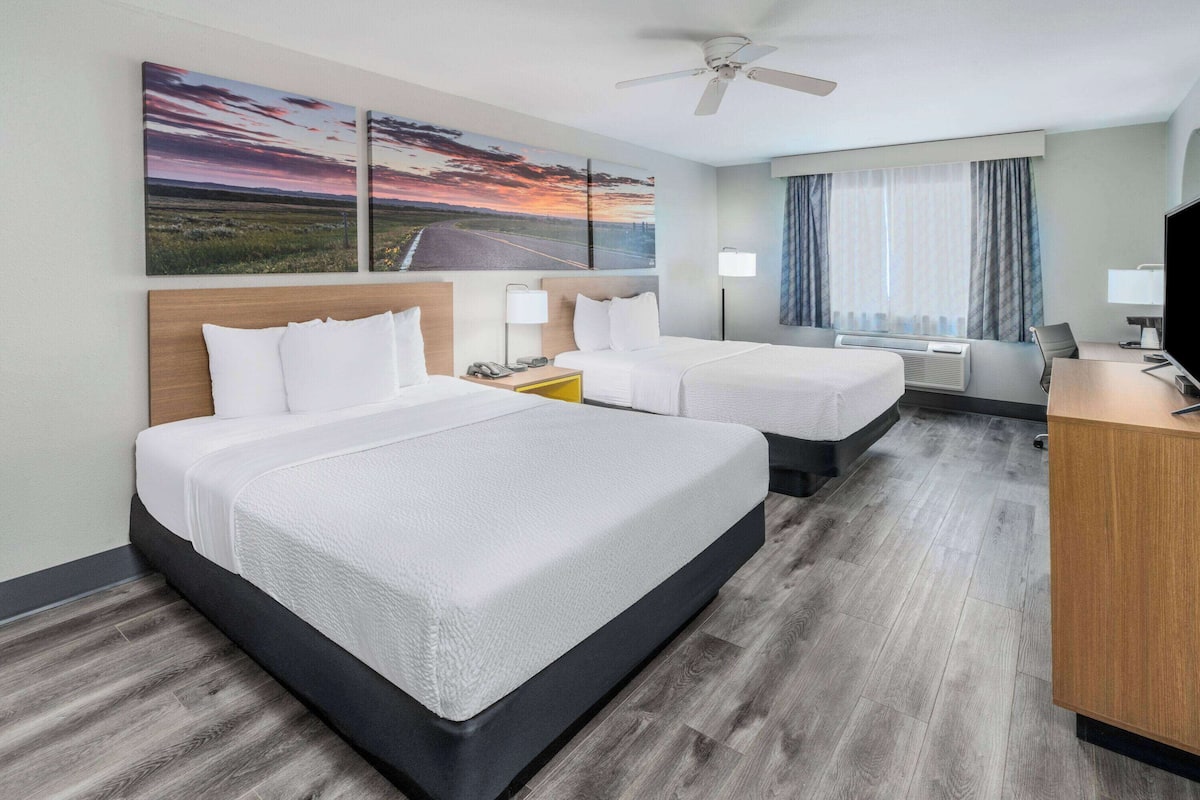A hotel room with two beds, a desk, a television, and a ceiling fan.
