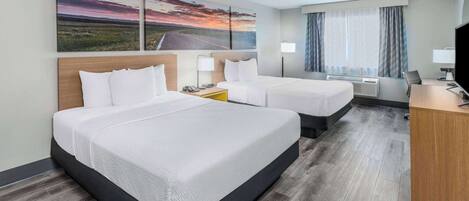 Habitación de hotel con dos camas, un escritorio, un televisor y un ventilador de techo.